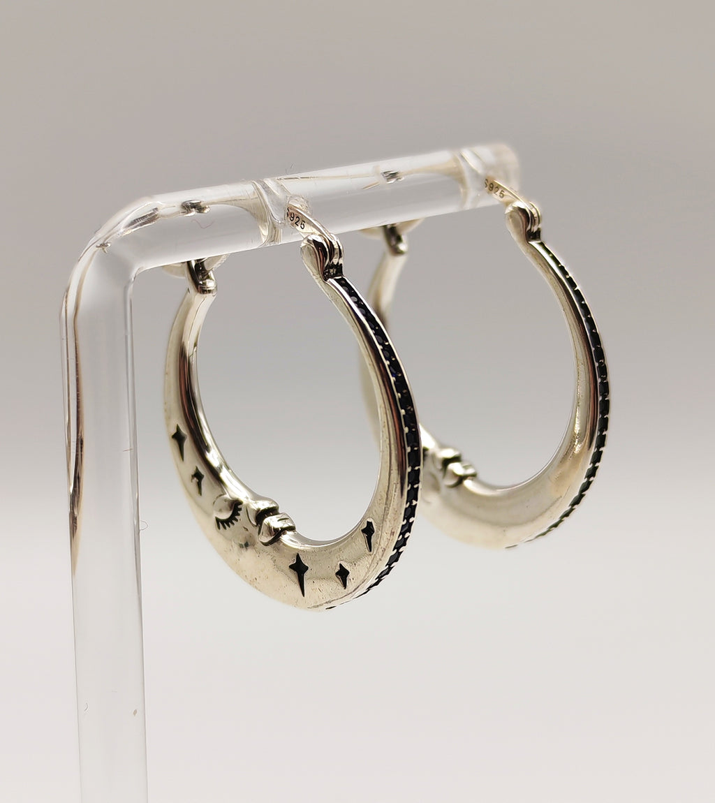 Sterling Silver half moon hoop earrings on a clear stand against a light gray background.