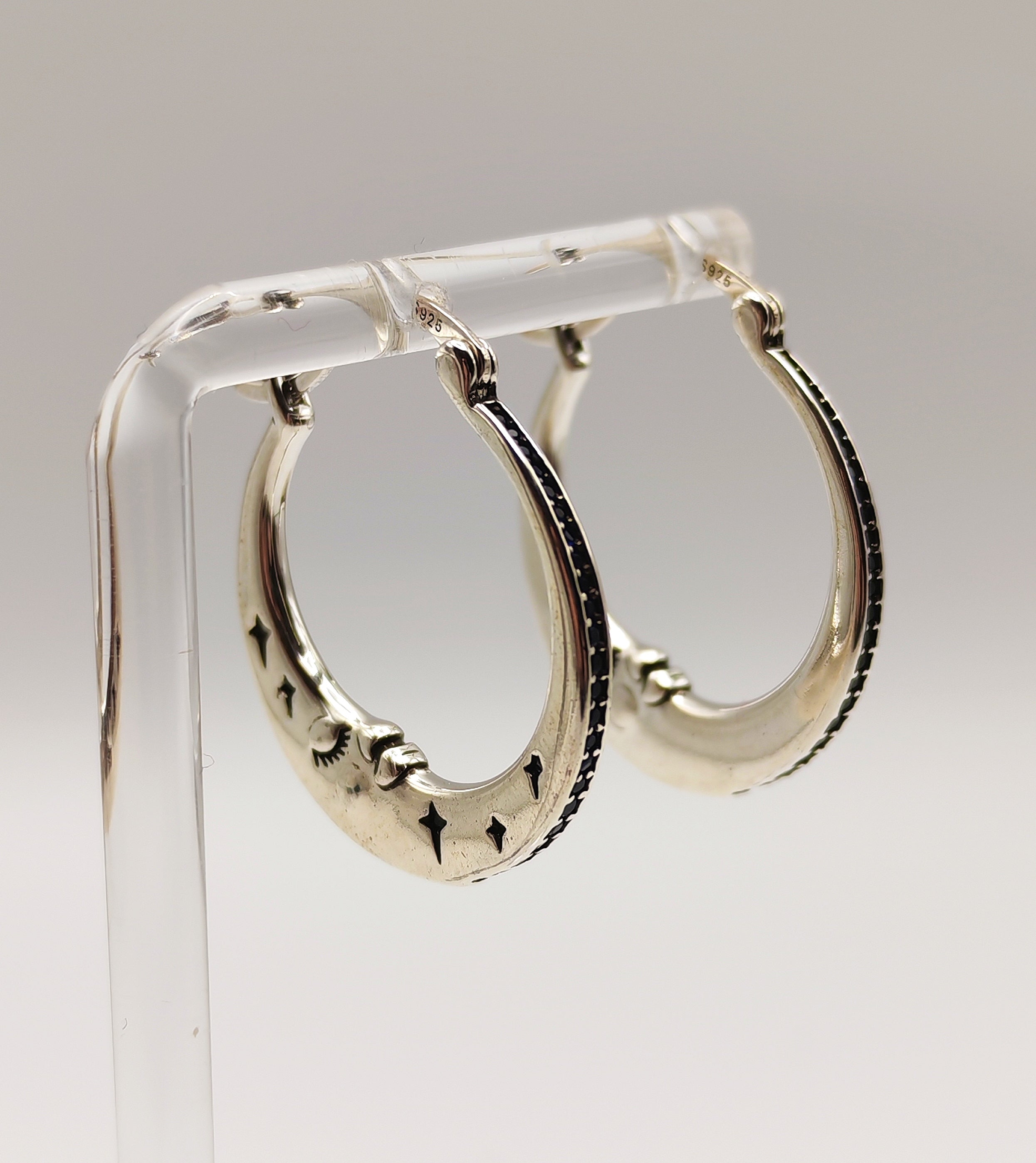 Sterling Silver half moon hoop earrings on a clear stand against a light gray background.