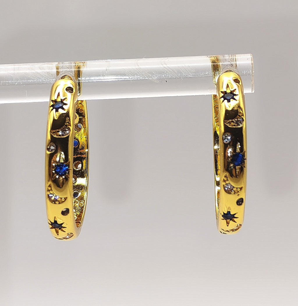 Close-up of gold plated star-pattern hoop earrings showing blue and white zirconia detailing.