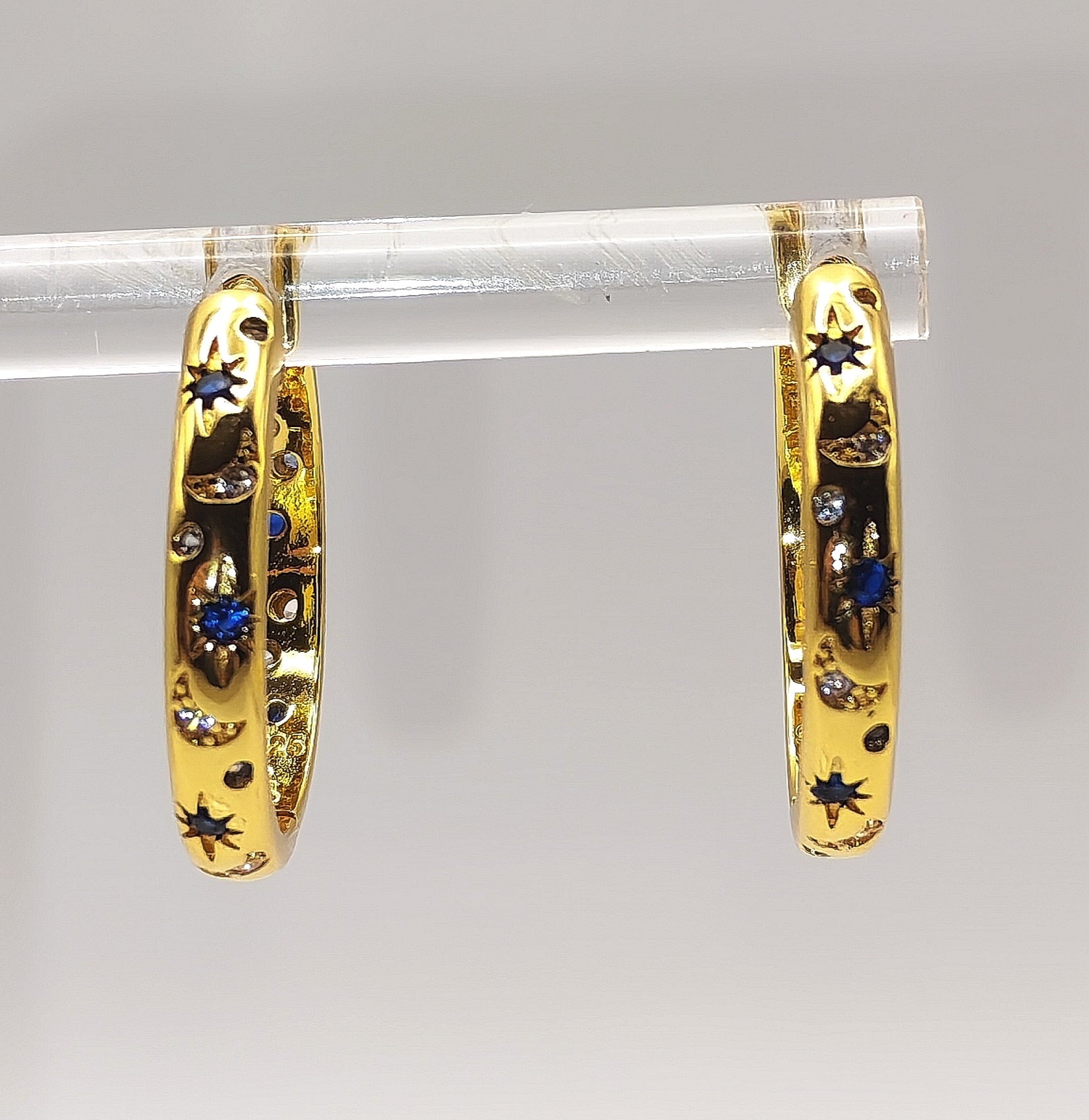 Close-up of gold plated star-pattern hoop earrings showing blue and white zirconia detailing.