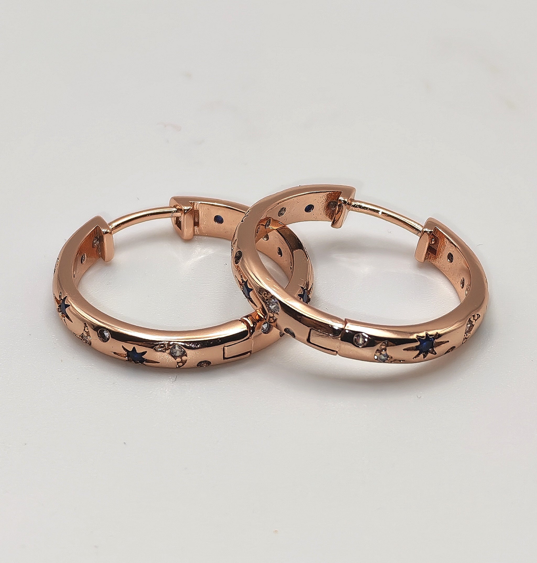 Rose gold plated sterling silver hoop earrings with blue and white zirconia's displayed on a white background.