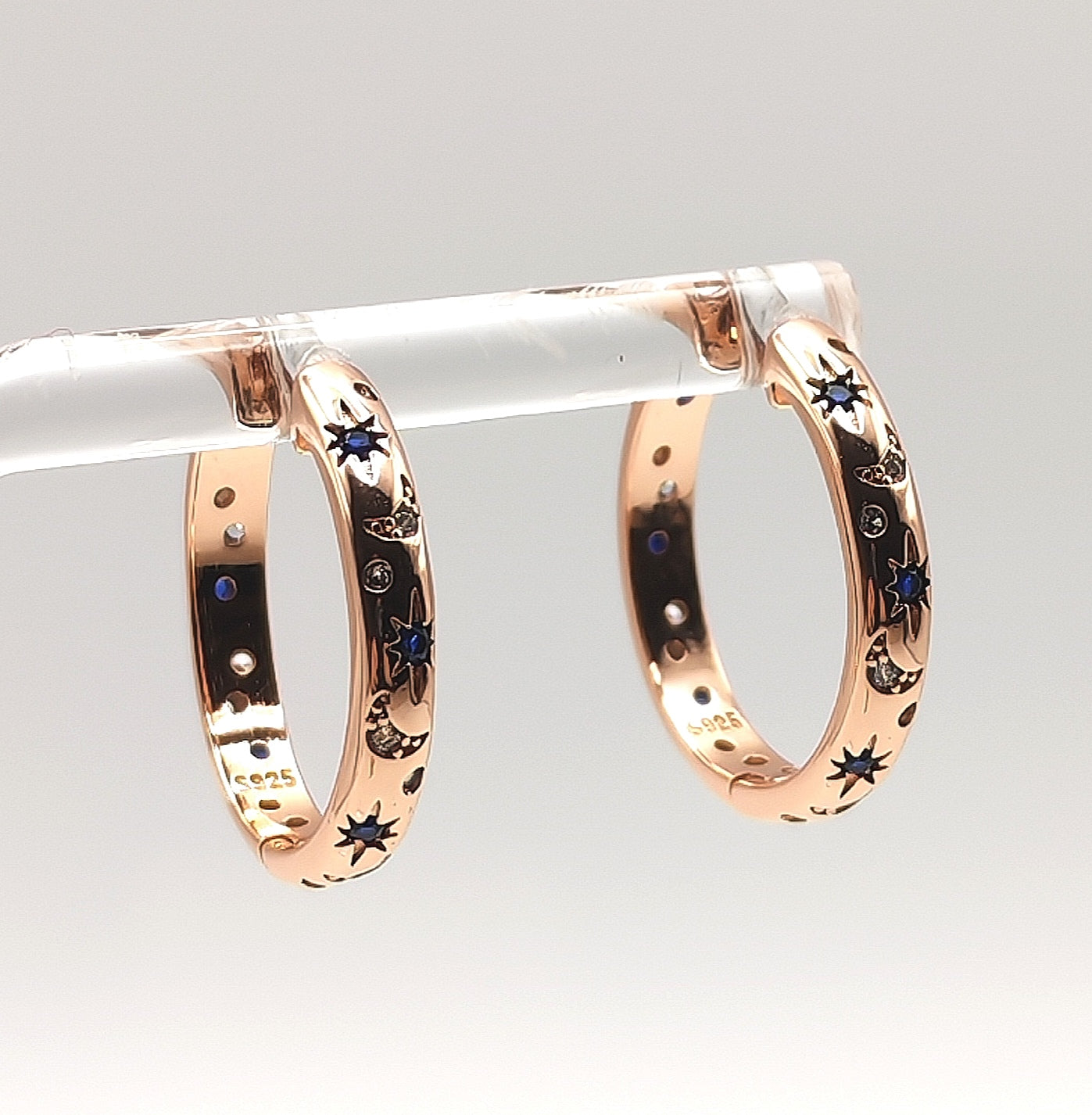 Close-up of rose gold celestial hoop earrings showing blue and white zirconia star and moon detailing.
