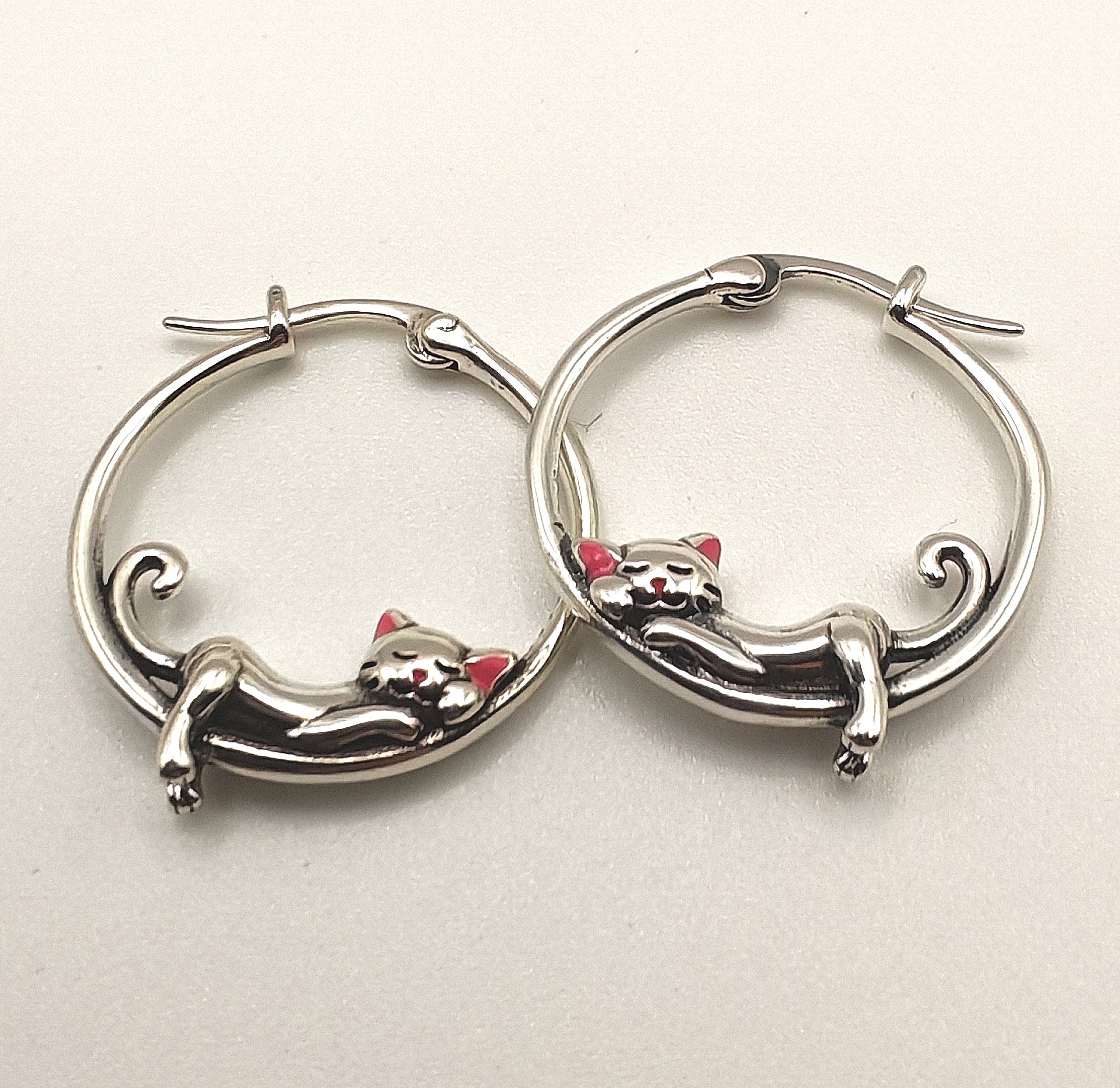 Macro shot highlighting the fine detailing of the sterling silver sleeping cat on the hoop earring.