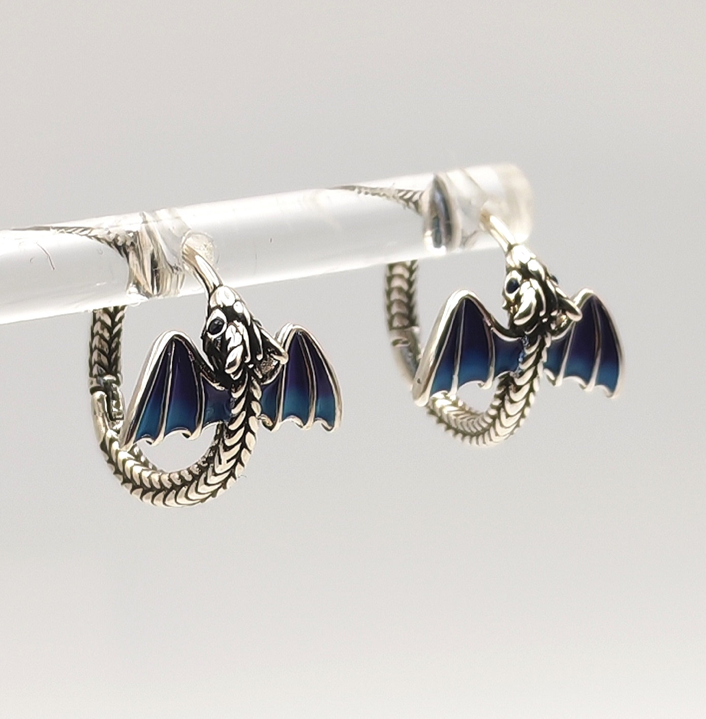 Sterling silver dragon hoop earrings with blue enamel wings on display stand