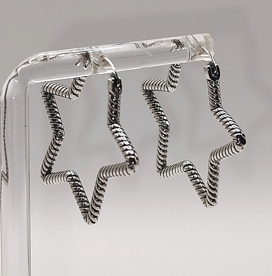 Silver spiral earrings on a clear stand against a gray background