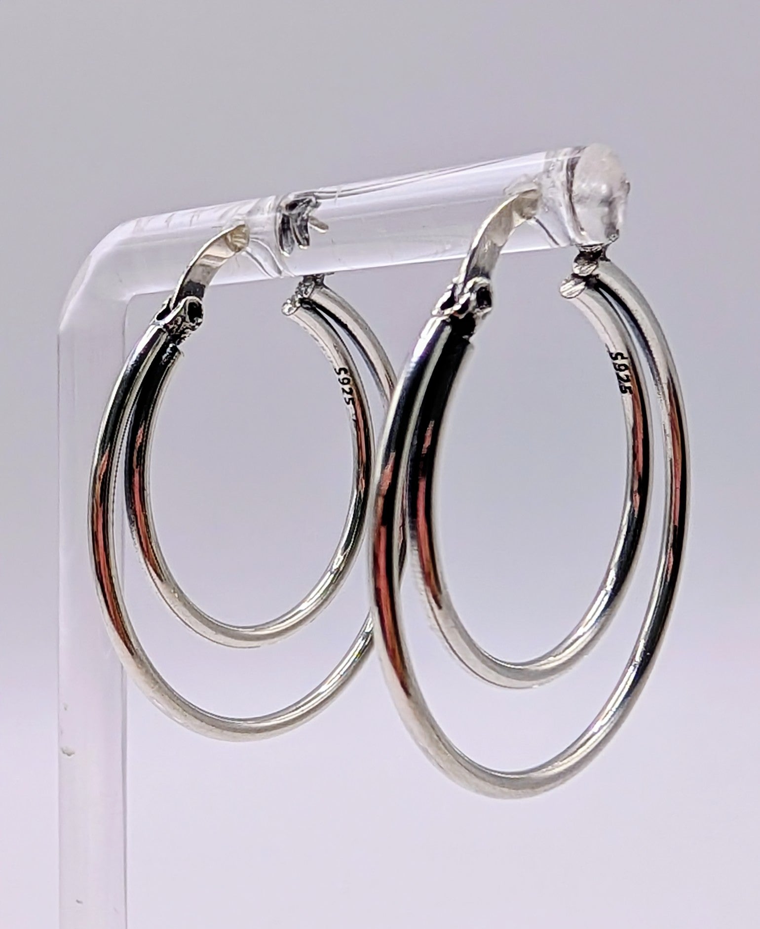 Sterling silver double hoop earrings displayed on a clear stand against a plain background