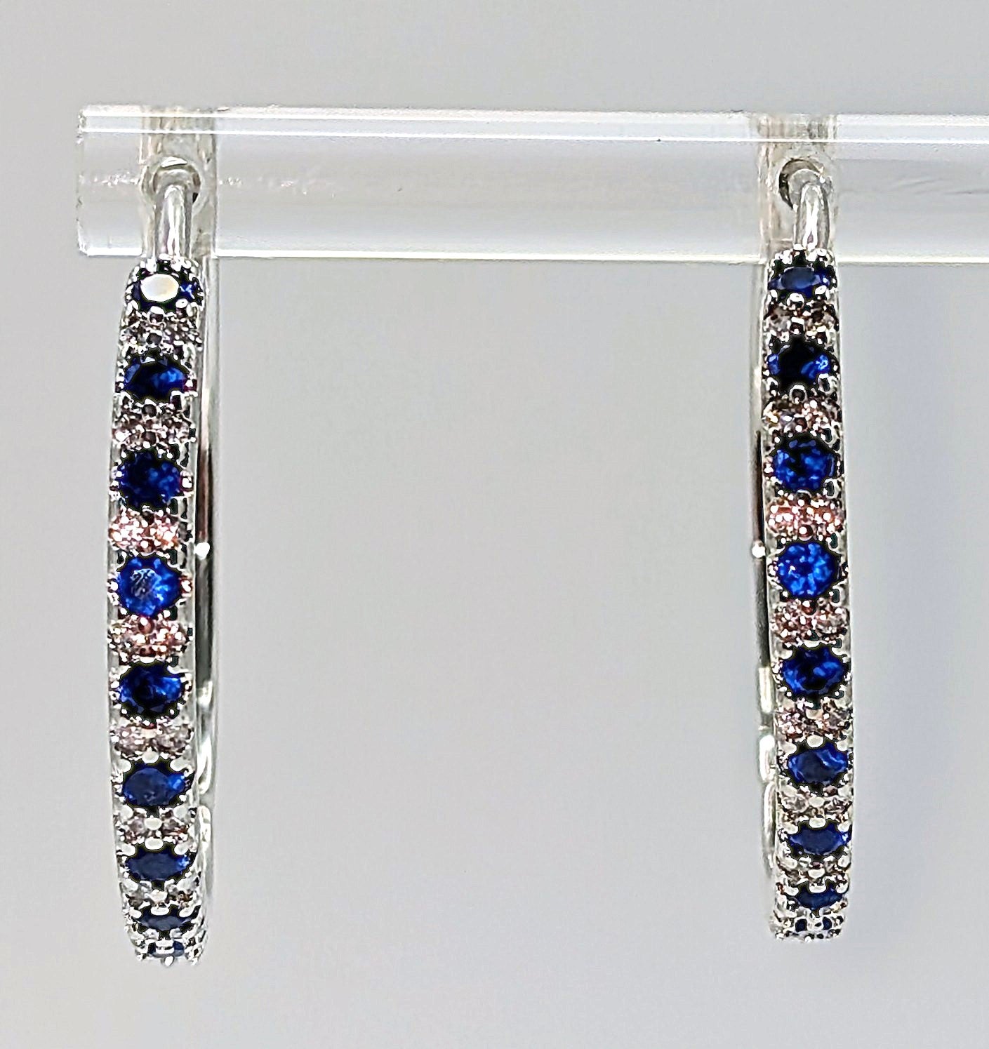 Sterling silver hoop earrings with blue and clear zirconia stones on white background