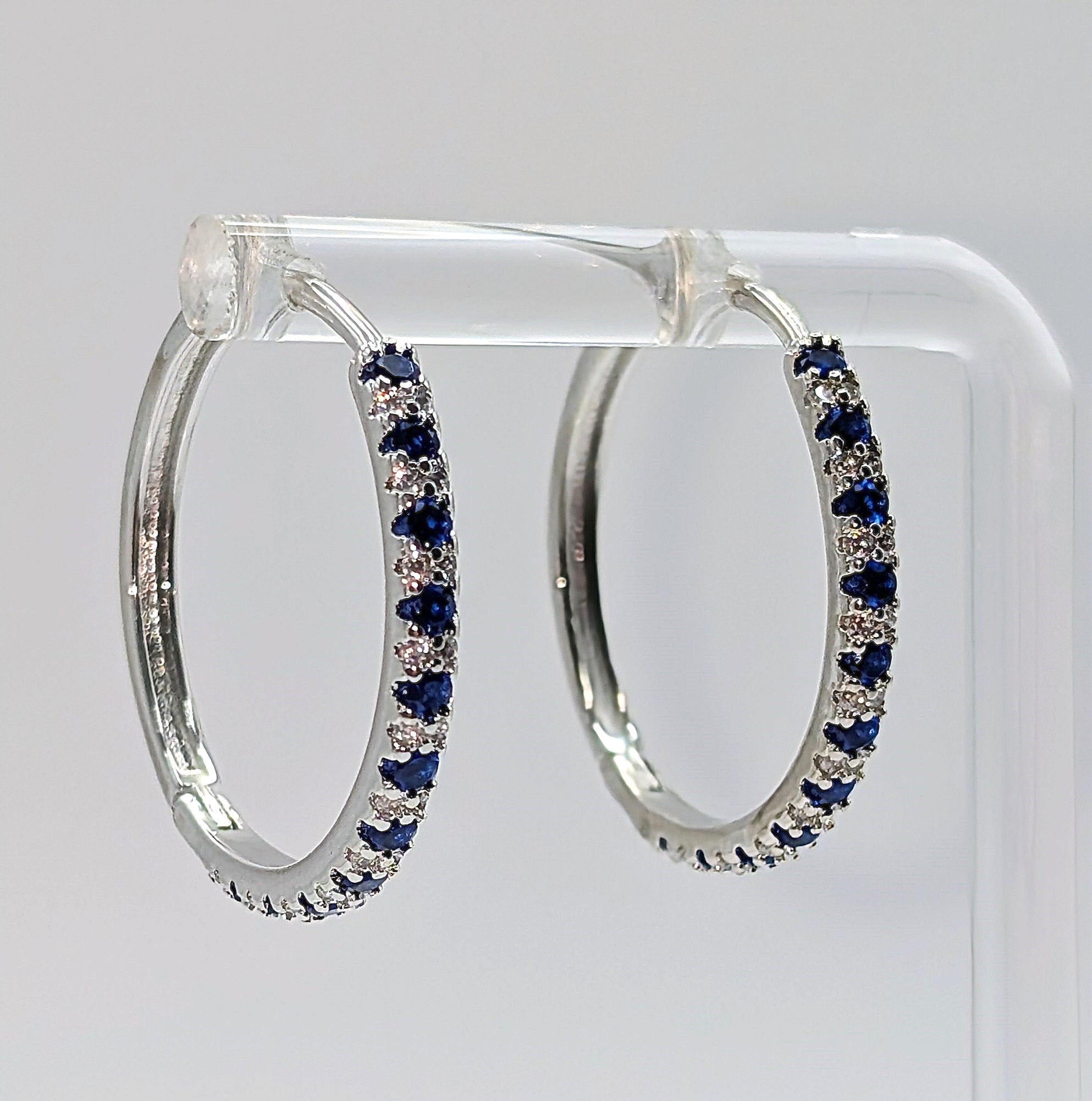 Sterling silver hoop earrings with blue and clear zirconia stones on white background