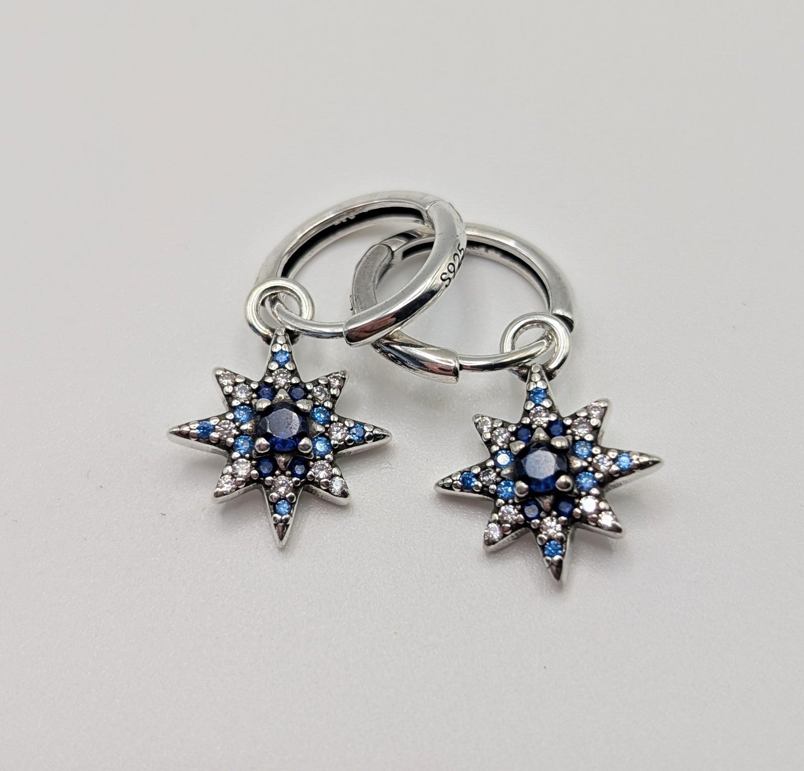 Close-up of silver hoop earrings with star charm and blue zirconia
