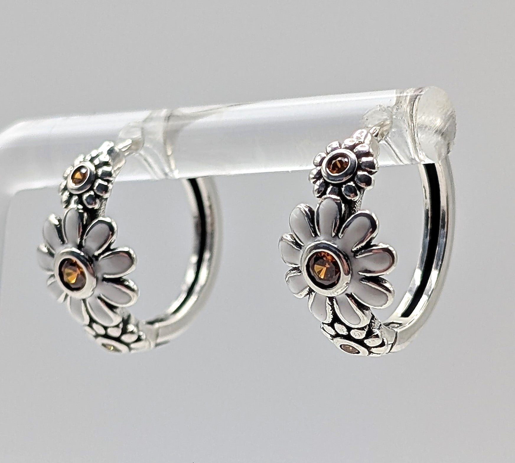 Sterling silver daisy hoop earrings with amber zirconia stones on display stand